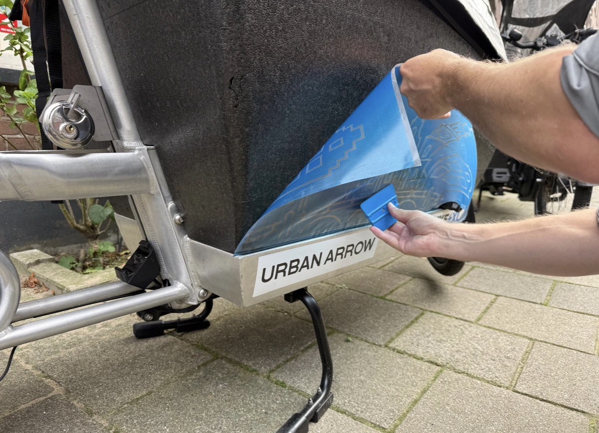 Een vinyl verfsjabloon wordt met transferfolie aangebracht op de EPP-bak van een Urban Arrow bakfiets